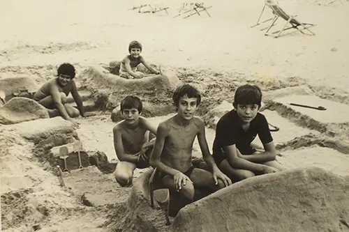 Cinque bambini che fanno costruzioni con sabbia e palette negli anni 70